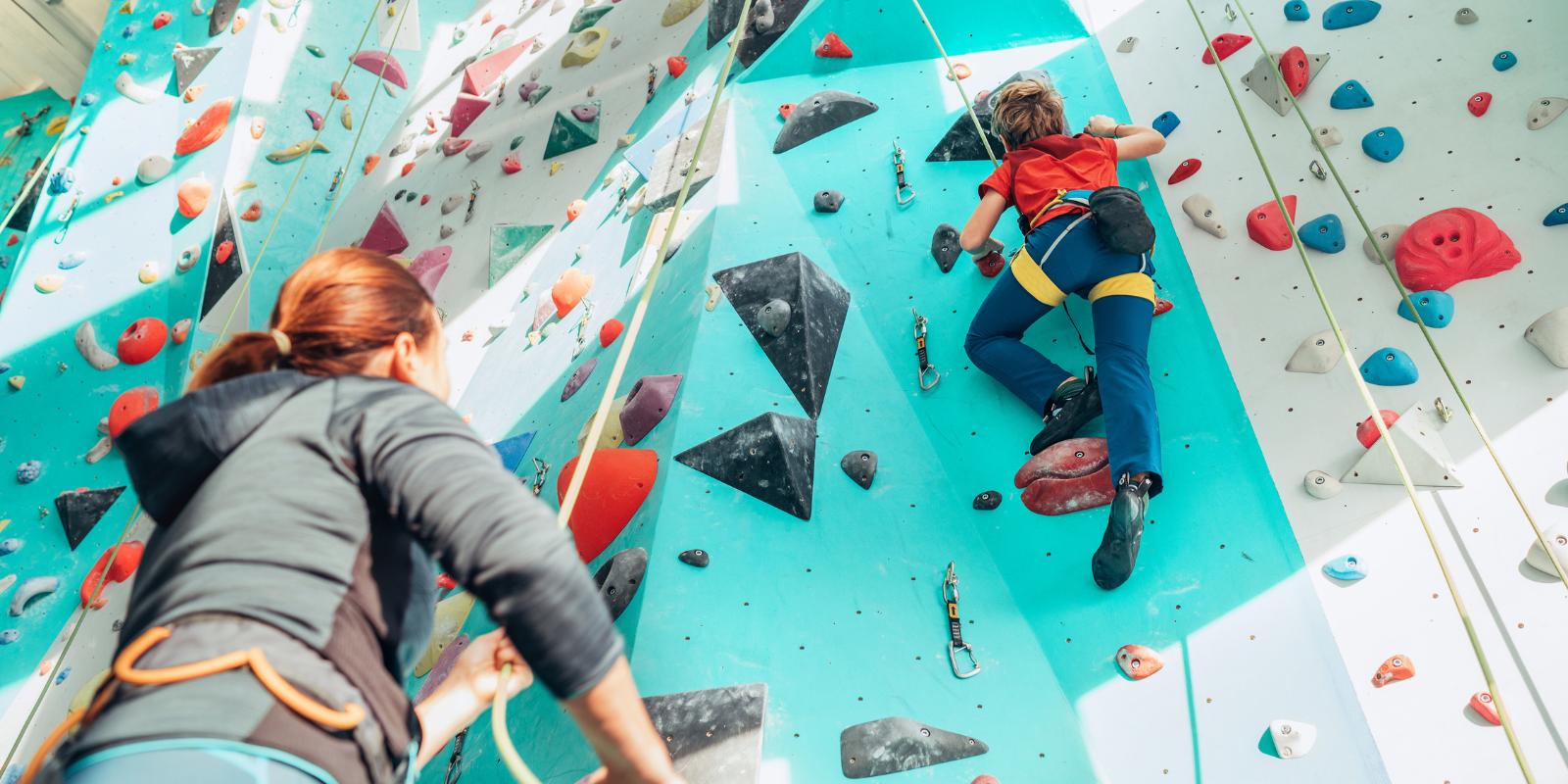 Parent watching helping child climb indoor rock wall. 